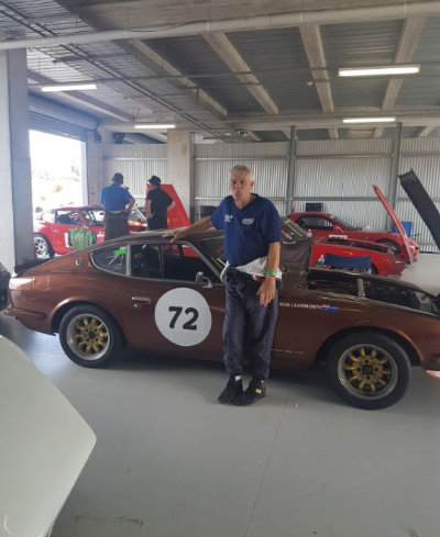 Robert Learmonth standing beside his bronze Datsun competition car bearing race number 72.